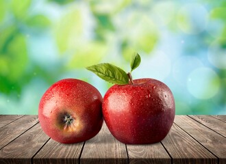 Two red apples with green leaves on outdoor background