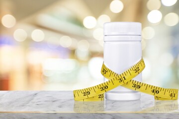 A jar with tablets in capsules stands in front of a measuring tape. The concept of weight loss, fat...