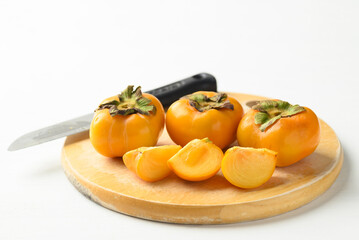 Sliced ripe persimmon fruit on cutting wooden board on white background