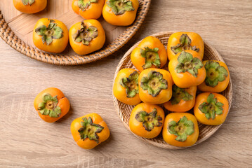 Ripe persimmon fruit in basket on wooden background, Table top view