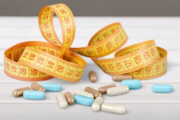 A Set tablets in capsules stands in front of a measuring tape. The concept of weight loss, fat burner, vitamins, sports nutrition.