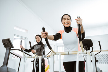 two beautiful woman with hijab at the gym exercising with friend on static elliptical cycle machine...