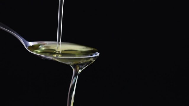 Close-up  slow motion pouring golden hemp oil liquid into spoon on  black background,  Herbal Treatment, Alternative Medicine.