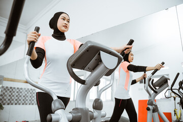 muslim women at the gym doing cardio exercises on static elliptical cycle machine