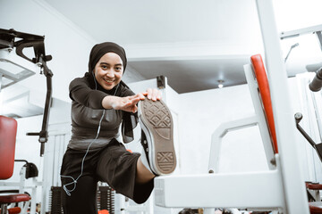 Attractive sports muslim girl smiles and looks at the camera while stretching her body in the gym,...