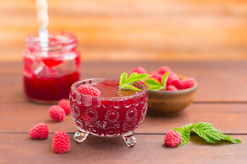 fresh raspberry jam in a glass jar on a wooden table, next to fresh raspberries. concept of homemade jam, preserves for winter, selective focus