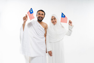 Excited couple wearing ihram clothes carrying Malaysian flag on isolated background