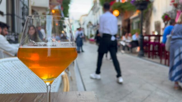 A nice cold beer in a busy tourist street during summer in Marbella old town Spain, blurry people sitting and having food outside in restaurants, 4K shot
