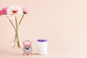 women health concept. medicine, health care style. copy space. white plastic bottle with pills, flowers and clock on beige background. 