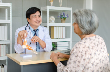 Asian cheerful male professional doctor practitioner in white lab coat with stethoscope sitting smiling holding showing foot skeleton model explaining to old senior female patient in clinic office