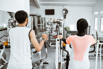 muslim couple using elliptical cycle machine for exercising together at the gym