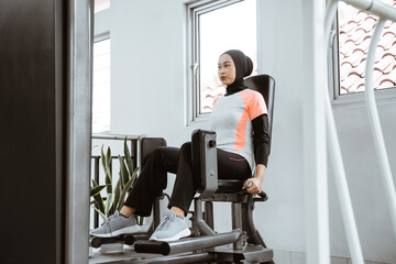 muslim asian woman working on her lower body using leg machine at the gym