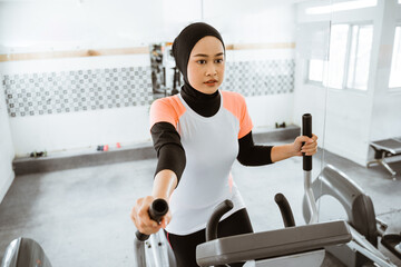 muslim women at the gym doing cardio exercises on static elliptical cycle machine