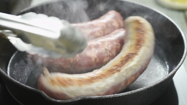The cook turns the sausages into the frying pan with a cooking tongs.
