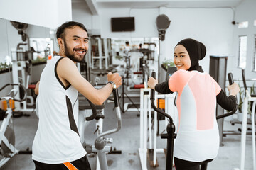 muslim couple using elliptical cycle machine for exercising together at the gym
