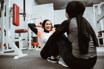 beautiful muslim woman sitting up exercise with partner at the gym