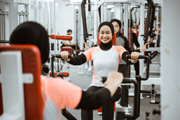 Fototapeta na wymiar beautiful muslim asian woman using chest press machine during fitness at the gym with friend