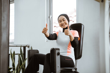 muslim asian woman working on her lower body using leg machine at the gym thumb up