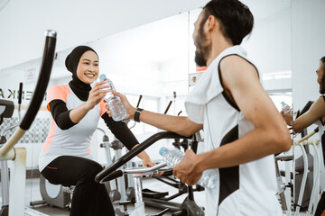 muslim couple exercising together at the gym having a bottle of water while taking a break
