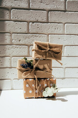 A set of handmade gifts in kraft paper, tied with wide twine, decorated with dry flowers on a white table. Front view