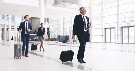 Group of formal business people walking through a busy airport hall pulling their trolley bags. Businessman with colleagues smiling on the phone, before the departure to the working trip. - Powered by Adobe