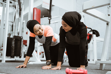 asian muslim woman doing plank push up with partner at the gym