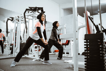 two beautiful muslim woman stretching and exercising at the gym together