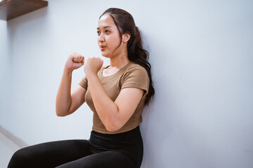 portrait of young asian woman squating against the wall at home