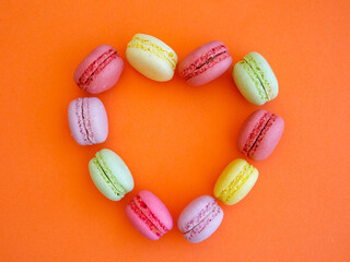 Obraz na płótnie Canvas Delicious colorful Macarons almond cookies shape of heart on orange background
