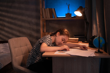 girl student falls asleep at the table at night, tired child sleeps at desk in the bedroom