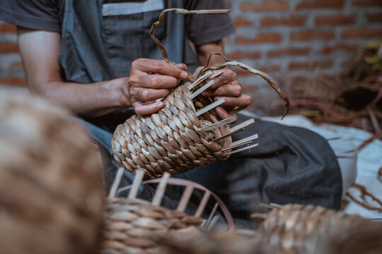 close up of male entrepreneur hands weaving water hyacinth into crafts on a brick house background