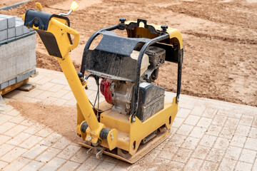 Vibratory rammer with vibrating plate on a construction site. Compaction of the soil before laying paving slabs. Close-up.