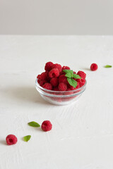 Fresh raspberries in the clear glass bowl on the white background