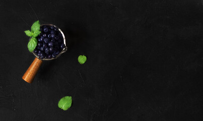 Fresh forest blueberries in a ladle with wooden handle on a black background with copyspace. Flatlay, top view. Close up.
