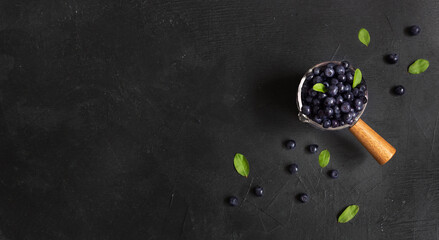 Fresh forest blueberries in a ladle with wooden handle on a black background with leaves. Copyspace. Flatlay, top view. Close up.
