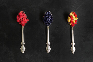 Three spoons with berries (raspberries, blueberries, strawberries) on the black background. Closeup. Flatlay.