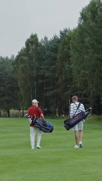Rear view of two men walking across a golf course with gear bags on their backs