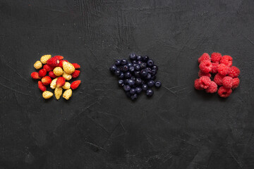 Three handfuls of berries (raspberries, blueberries, strawberries) on a black background. Closeup. Flat lay.