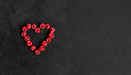 The heart from the raspberies on the black background with copyspace