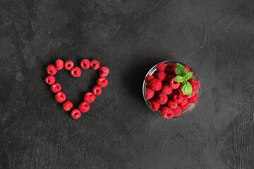The raspberies heart and fresh raspberries in the clear glass bowl on the black background