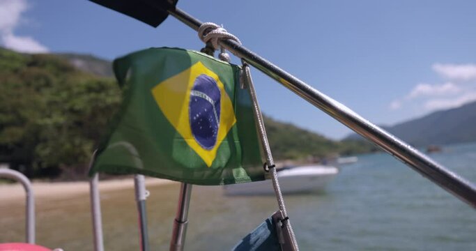 Brazilian flag flies on boat in front of tropical beach - close up
