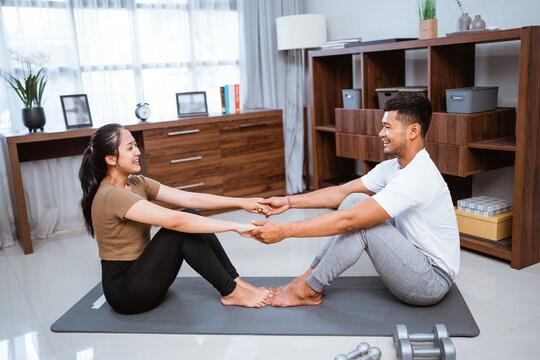 Asian fitness couple, man and woman exercising together at home doing yoga in livingroom facing each other