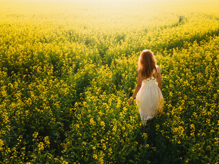 Woman in a long yellow dress walking on the field with yellow flowers at sunset.