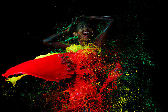 Happy smile Sensual sexy woman and colorful paint splashes on black studio room background.