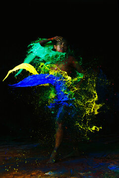Sensual sexy woman and blue, yellow, green paint splashes on black studio room background.