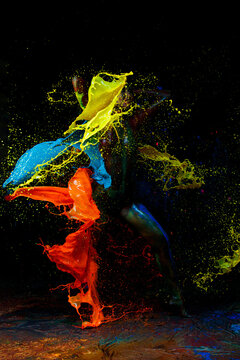 Color spash. Sensual sexy woman and colorful paint splashes on black studio room background.