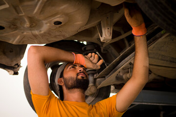 Pakistani or Indian Mechanic under a car giving maintenance service