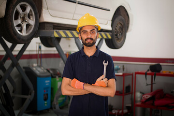 Pakistani or Indian Mechanic holding wrench in hand standing in garage