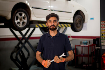 Fototapeta na wymiar Pakistani or Indian Mechanic holding wrench in hand standing in garage