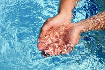 The hands cupped together submerged in clean clear blue water in swimming pool